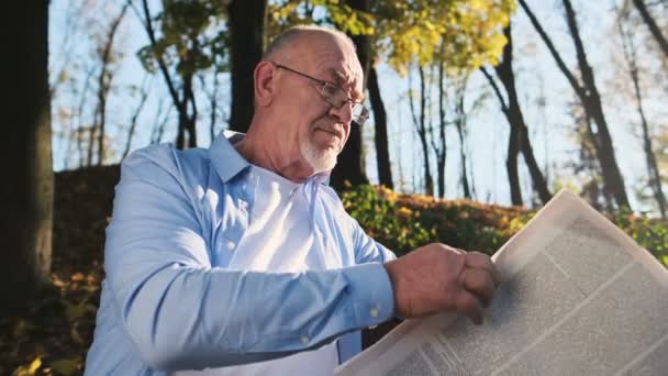 Retraite active, homme âgé barbu et portant des lunettes lisant le journal dans le parc . — Video