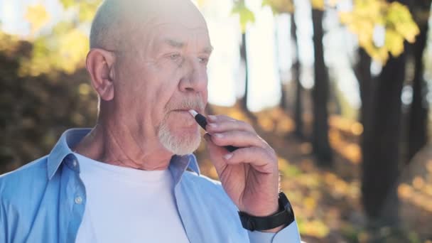 Nahaufnahme eines älteren Mannes, der eine elektronische Zigarette genießt. iqos. Bärtiger Mann raucht neue E-Zigarette im Park — Stockvideo