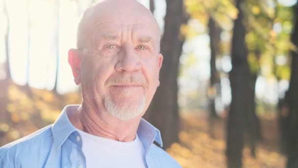 Close up portrait of senior man with a beard smiling while standing outside in sunlight. — Stock Video