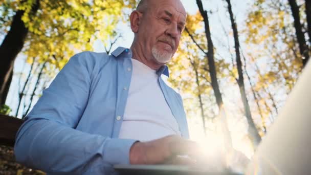 Gros plan portrait de l'homme âgé avec une barbe à l'aide d'un ordinateur portable en plein air. Père est assis sur un banc de parc et utilise un ordinateur hir . — Video