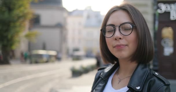 Ein Mädchen lächelt auf der Straße. niedliche Dame mit Brille lächelt auf der Straße, Nahaufnahme — Stockvideo