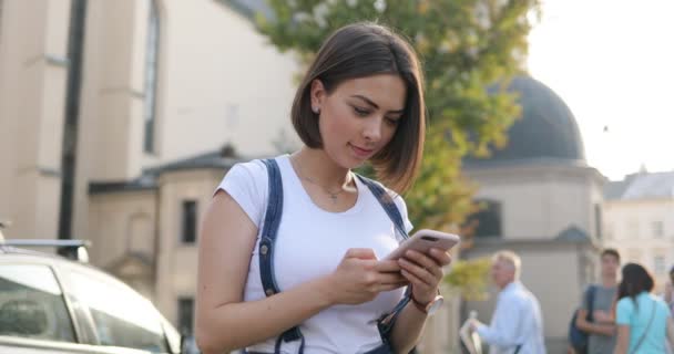 Ein nettes brünettes kaukasus-mädchen tippt auf ihrem telefon auf der straße von europa — Stockvideo