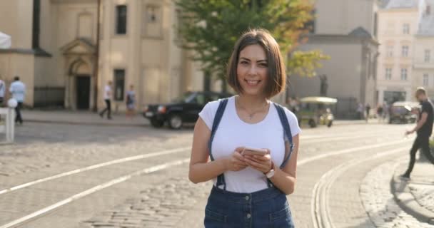 Een meisje houdt een telefoon is haar handen en glimlachen naar de camera — Stockvideo