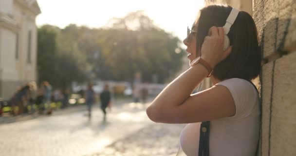 Una chica está tomando sus auriculares en la calle — Vídeo de stock