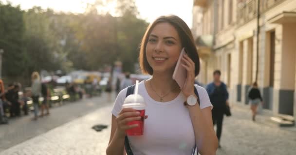Una chica está caminando y hablando en su teléfono al aire libre — Vídeo de stock