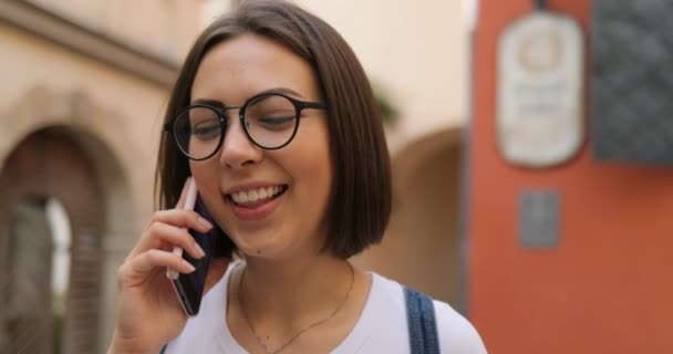 Una chica con gafas habla por teléfono y se ríe. — Vídeos de Stock