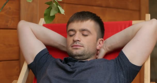 A man on a deckchair is having rest, close-up. A man on a deckchair is having rest and his son plays with a branch around dads face — Stock Video