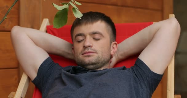 Člověk spí na relaxačním, když jeho syn probudí ho, detail. Muž na relaxačním má odpočinek a jeho syn hraje s větví kolem obličeje tatínky — Stock video