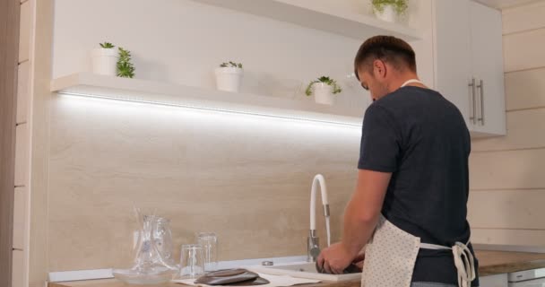 Ein Mann spült das Geschirr. ein glücklicher Mann spült das Geschirr in einer schönen, hellen Küche — Stockvideo