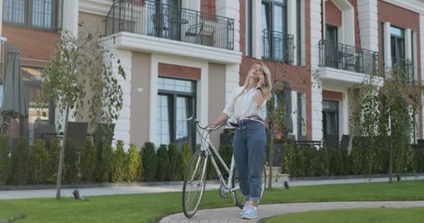 自転車で携帯電話 スマート フォンでのテキスト メッセージのアプリを使ってかわいい金髪の女の子 街の通りで自転車を持つスタイリッシュな女 — ストック動画