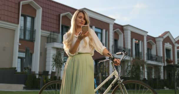 Красиві щасливі молода дівчина з vintage велосипед говорити на смартфоні, усмішки на камеру і сміючись, стоячи над європейські будівлі. Hipster за допомогою смарт-телефон зовнішніх, річна дівчина портрет — стокове відео