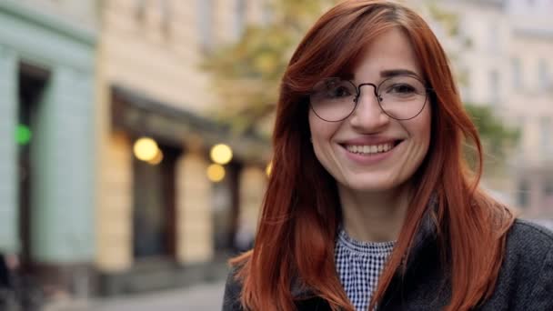 Feche o retrato da mulher jovem que sorri com o cabelo vermelho em óculos. Menina atraente sorrindo e olhando para a câmera, confiante bonita — Vídeo de Stock