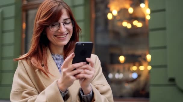 Retrato da mulher caucasiana de negócios de Nealitz com mensageiro de mensagens de texto de smartphone. Menina cabeça vermelha atraente usando aplicativo no telefone móvel. Mulher percorre um site de mídia social usando telefone inteligente . — Vídeo de Stock