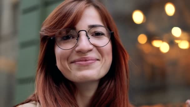 Close up retrato de atraente sorridente etnia caucasiana jovem gengibre mulher vestindo óculos em ambiente urbano. Menina sorrindo e olhando para a câmera na cidade, confiante bonita . — Vídeo de Stock