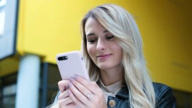 Genç kadın sarı bina ve smartphone kullanarak yakın duruyor. Akıllı telefon teknoloji app şehirde yürüyüş kullanan güzel kız. Kadın manifatura, tarama ve akıllı telefon online alışveriş