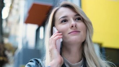 Gülümseyen mutlu kadın bir cep telefonu kullanarak. Mutlu genç kız bardaklarda sevgilisi için sokakta yürürken cep telefonuyla konuşuyor. Portre, yaşam tarzı, kentsel kapatın