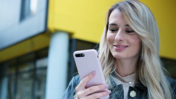 Close-up retrato de mulher na cidade usa smartphone ao ar livre. Muito hipster, estudante mensagens de texto menina e usando o aplicativo no telefone inteligente no fundo amarelo. Estilo de vida, urbano — Vídeo de Stock