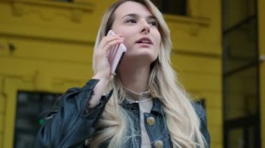 Açık havada smartphone kullanarak bir molada genç çekici kadın portresi. Uzun saçlı görüşmeleri o cadde boyunca yürür iken telefon ile sarışın kız. Portre, yaşam tarzı, kentsel kapatın
