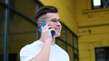 Akıllı telefon kullanan rahat genç adam. Smartphone gülümseyen açık havada beyaz t-shirt giyen mutlu konuşan adam portresi