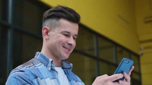 在城市智能手机上使用商业应用的人的肖像。英俊的年轻人在智能手机上交流微笑自信。城市高加索男性通勤 — 图库视频影像