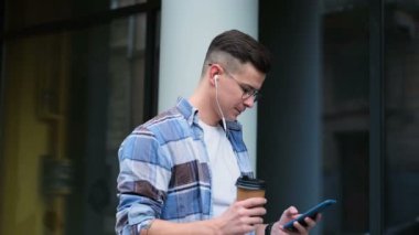 Smartphone emin gülümseyen iletişim yakışıklı delikanlı. Adam caddenin üzerinde tek kullanımlık kağıt bardak kahve içme smartphone ile portresi