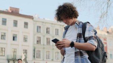 Yakışıklı delikanlı, turistik veya öğrenci, hippi kıyafet, bin yıllık onun smartphone kullanarak sosyal medya harita kontrol veya app, etrafa haber okuma aygıtında besleme yoluyla kayar