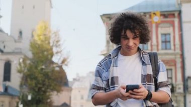 Portre çekici bir genç adam, turistik veya öğrenci, nesil z ya da bin yıllık hipster kıyafeti, sosyal medya veya oyun uygulamaları, dikkati haber içine bakar besleme smartphone
