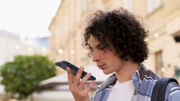 Homem usando uma função de reconhecimento de voz de telefone inteligente on-line andando em uma rua da cidade, falando com assistente móvel. Turista usando reconhecimento de voz de telefone inteligente, dita pensamentos, mensagem de marcação de voz — Vídeo de Stock