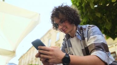 Müzik ve smartphone üzerinde tarama gülümseyen adam akıllı telefon, kullanarak kulaklık. Açık. Yakın çekim. App haber okuma aygıtında, sosyal medya aracılığıyla Blogger kayar