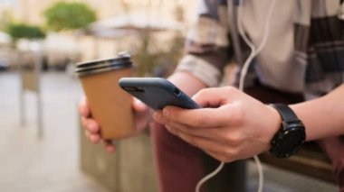 Smartphone kullanarak ve kahve içme adam açık gitmek için. Yakın çekim. Nesil z hipster kıyafeti, onun smartphone kullanarak sosyal medya aygıtta, harita, haber app üzerinde okuma kontrol besleme yoluyla kayar