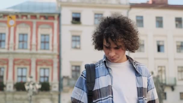 Sokakta yürüyen şık yakışıklı kıvırcık genç adam portresi. Hipster gülümseyen, blogger smarphone kullanarak, aygıtta yem ve kahve tutan sosyal medya aracılığıyla kayar — Stok video