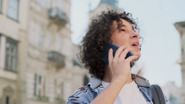 Gros plan portrait de jeune homme parlant sur smartphone. Heureux jeune homme décontracté utilisant un téléphone portable à l'extérieur, dans un centre-ville. Portrait d'un beau hipster parlant au téléphone et souriant . — Video