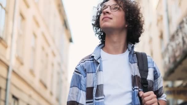 Nahaufnahme Porträt eines lächelnden und lachenden hübschen jungen Mannes. glücklich attraktive kaukasische Hipster, die nach draußen gehen und sich umsehen. Lockenkopf, Tourist oder Student im Hipster-Outfit vor der Kamera — Stockvideo