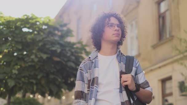 Ritratto di felice uomo caucasico carino sorridente in città. Bello giovane riccio, turista o studente, millenario in abito hipster, outdoor. Trendy uomo guardando la fotocamera — Video Stock