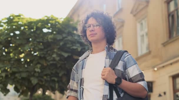 Portrait of happy cute caucasian man smiling in city. Handsome young curly man, tourist or student, millennial in hipster outfit, outdoor. Trendy man looking at camera — Stock Video