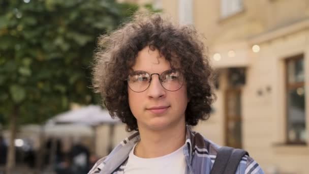 Close up portrait of happy cute caucasian man smiling in city. Handsome young curly man, tourist or student, millennial in hipster outfit, outdoor. Trendy man looking at camera — Stock Video