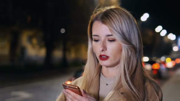 Mujer atractiva usando smartphone durante el paseo por las calles de la ciudad nocturna. Chica pidiendo un taxi. Servicio en línea taxi orden aplicación móvil. Taxi en línea, paisaje urbano . — Vídeos de Stock