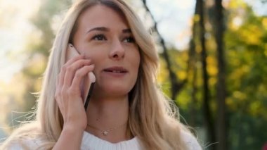 Sonbahar Park'ta yürüyüş smartphone üzerinde konuşmak güzel trendy beyaz kadının portresi kapatın. Beyaz kazak giyen kız cep telefonu, açık havada arama.