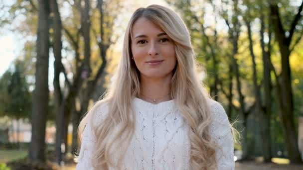 Gros plan portrait de la femme debout la lumière du soleil dans le parc d'automne. Au ralenti. Magnifique fille souriante avec un joli look et maquillage naturel en regardant la caméra — Video