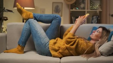 App kullanarak ve kanepe, güzel Bayan cep tarafından hoş komik konuşmayı yatan smartphone cep telefonu ile internet tarama kız gülümseyerek mutlu neşeli pozitif genç telefondaki kadın evde,