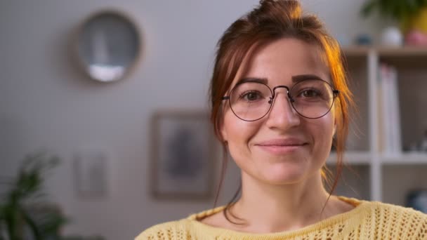 Close up face portrait of attractive young womanin eye glasses looking into camera in the living room at home. Beautiful girl smiling. Indoors. — Stock Video