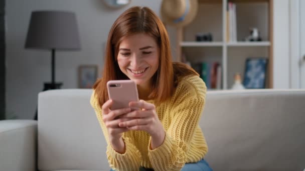 Молода успішна жінка використовує додаток для смартфона вдома у вітальні. Захоплена дівчина отримує хороші новини схвильована щасливою веселою посмішкою. Концепція успіху та досягнень — стокове відео