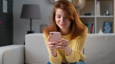 Gülümseyen ve gülerek mutlu kadın cep telefonu app, sohbeti kullanma online ile sokulgan ve sosyal medya için Bloglama rahat ev odasında otururken. Başarı ve başarı kavramı