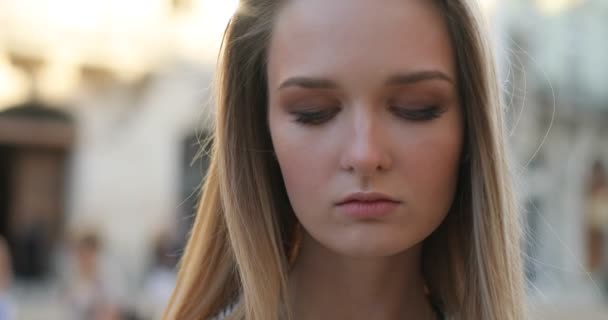 Retrato de una hermosa chica rubia mirando con sus ojos brillantes a la cámara con una cara seria al aire libre . — Vídeos de Stock