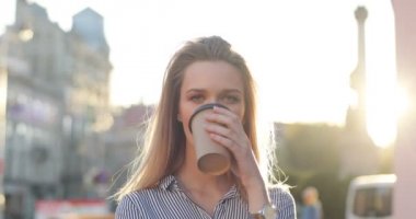 Güzel bir kız onu sabah kahve-to-go şehir merkezi ve gülümseyerek içiyor. Kameraya güzel bir gün. Önden Görünüm, yakın çekim.