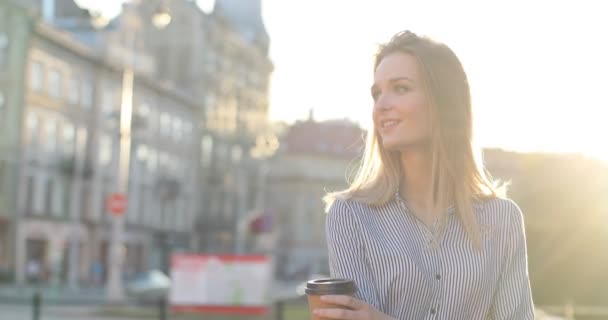 En vacker ung dam smuttar på sitt morgonkaffe på gatan och ler mot kameran. Närbild porträtt. — Stockvideo