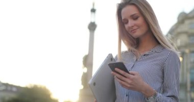 Yan görünümü portresi telefonunu ve arka plan üzerinde geçirerek arabalar kameraya gülümseyen güzel bir sarışın manifatura.