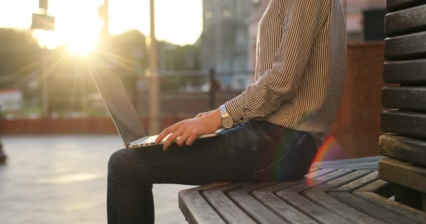 Una donna d'affari in camicia sta lavorando al suo portatile in panchina. Giorno pieno di sole, strada sullo sfondo . — Video Stock