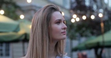 Bir kenara seyir ve yüzünü kameraya dönüm oldukça romantik bir kız portresi. Gece şehir ışıkları arka planda. Yakın çekim.