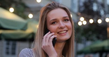 Genç güzel kadın telefona cevap ve sokakta akşamları gülümseyen. Sarışın mavi gözlü. Yakın çekim portre.